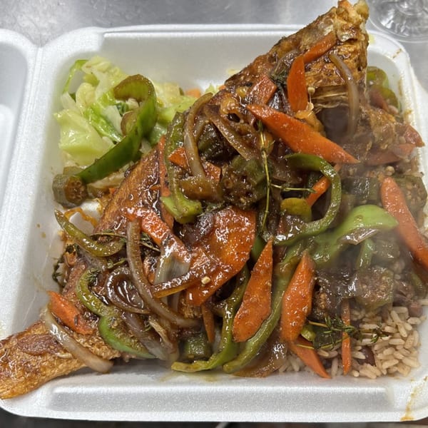 Steaming Jamaican escovitch fish with brown rice, cabbage, carrots, onions, and peppers in a takeout container.