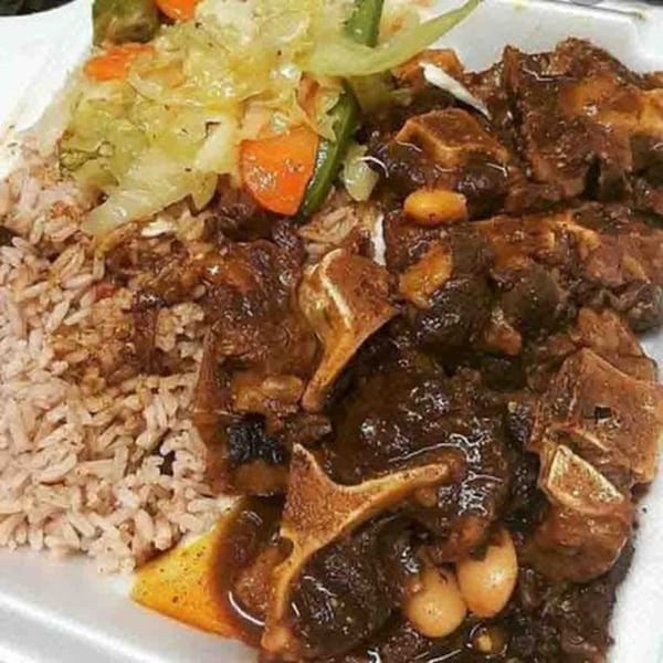 A plate of Jamaican oxtail stew with rice and peas, and steamed cabbage and carrots.