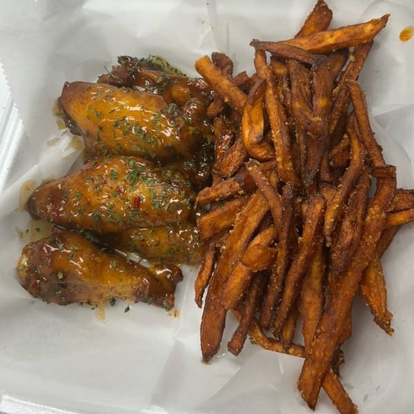 Island Flavors' jerk chicken wings with sweet potato fries, served in a white takeout container.