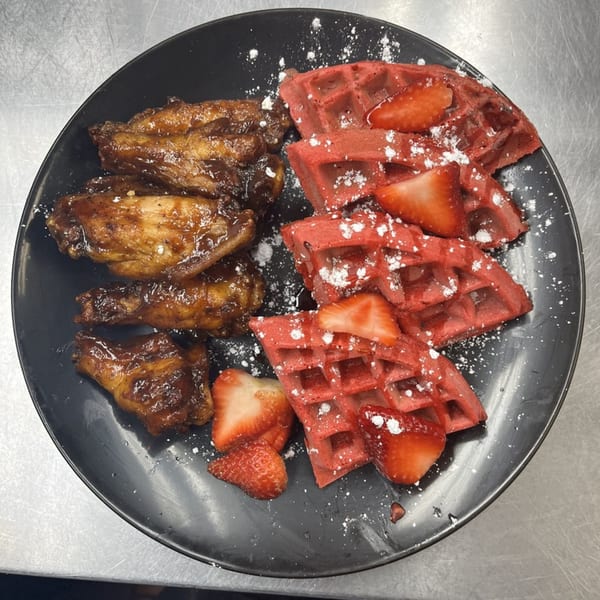 Island Flavors' chicken and waffles with red velvet waffles, glazed chicken wings, strawberries, and powdered sugar.
