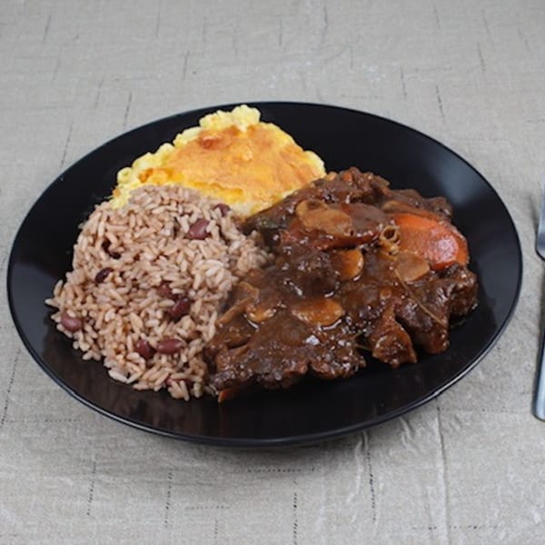 Island Flavors' Jamaican oxtail stew, rice and peas, and baked macaroni and cheese on a black plate.