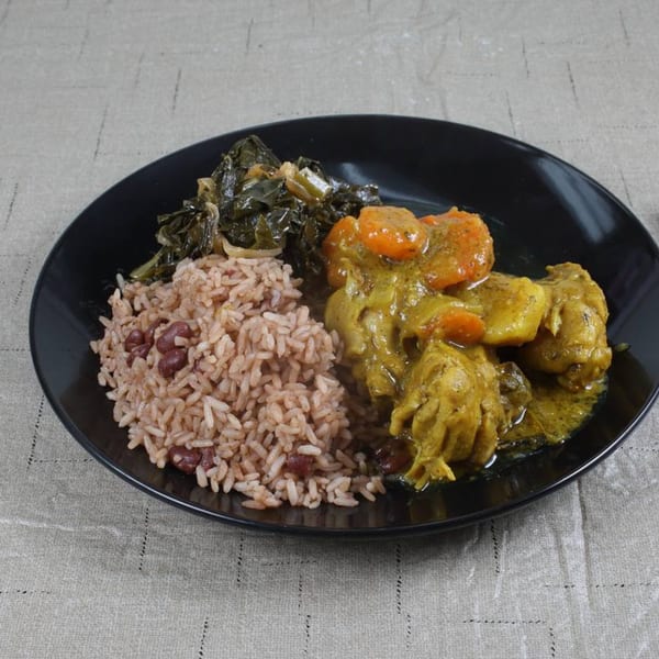 A black plate of Jamaican curry chicken, rice and peas, and steamed callaloo on a tablecloth.